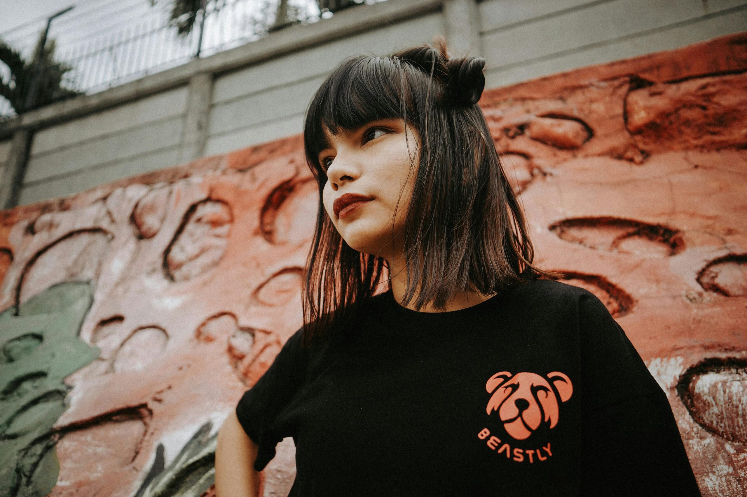 Asian woman in stylish Beastly t-shirt posing against urban graffiti wall.